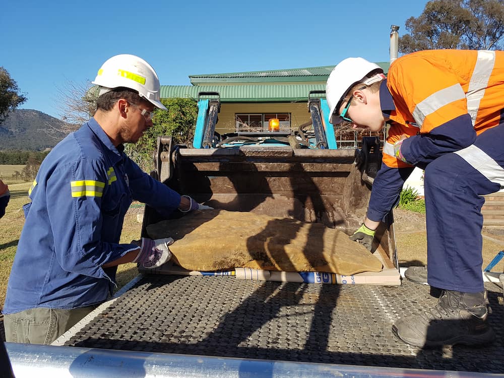 Two workers inspecting a rock on the back of a truck tray.