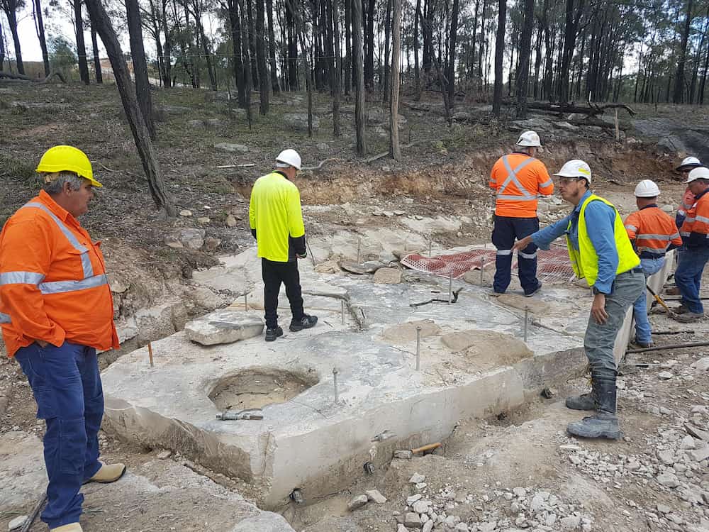 An excavation of a slab of stone with workers in high vis. 